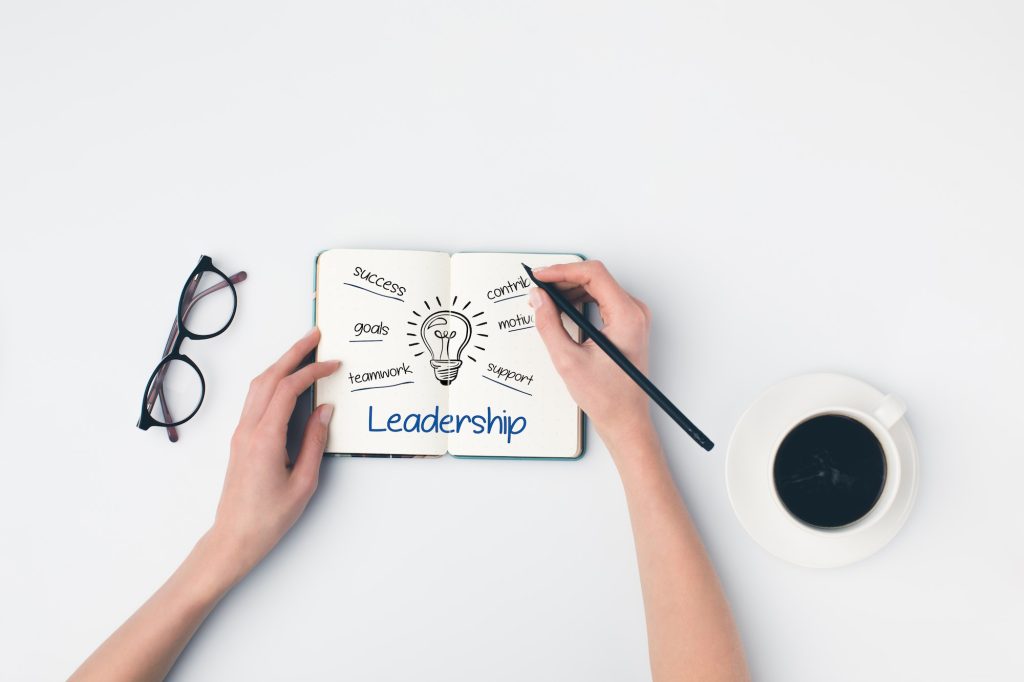 top view of woman writing leadership ideas in notebook on white table