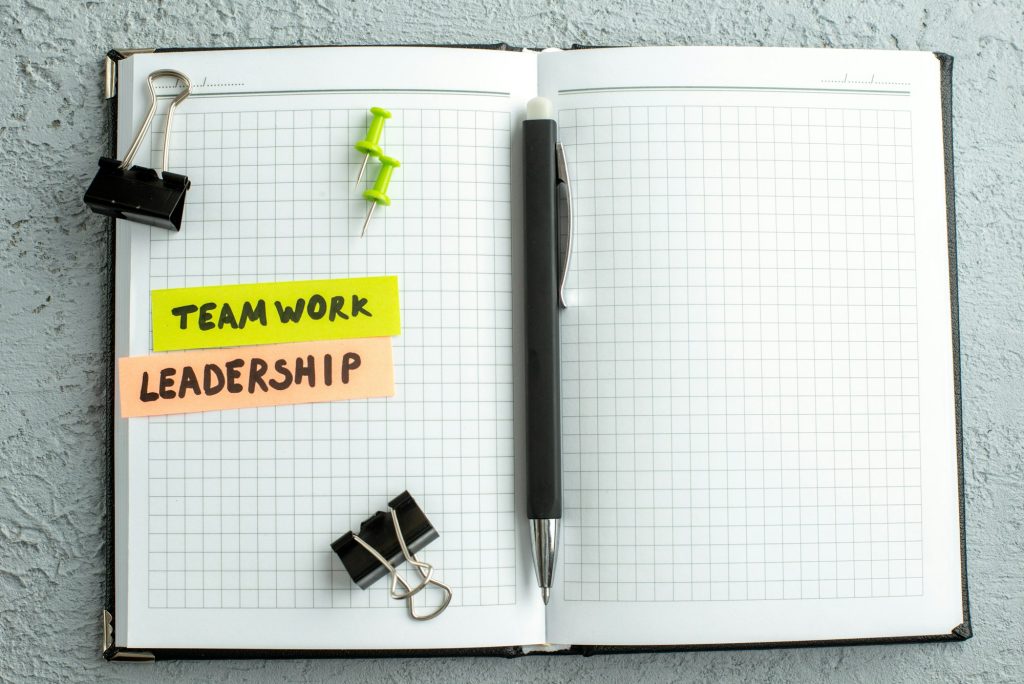 Above view of teamwork leadership writings pen and open spiral notebook on gray sand background