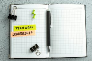 Above view of teamwork leadership writings pen and open spiral notebook on gray sand background